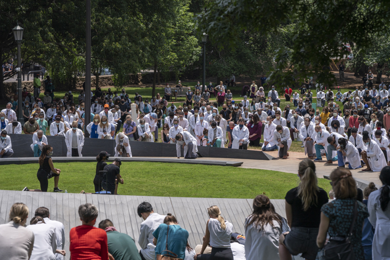 Medical staff in white coats kneeling next to memorial