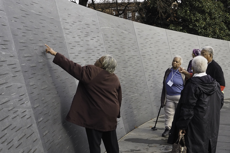 Person pointing at a spot on the memorial wall. 